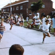 Oude foto van kinderen en supporters tijdens een loopwedstrijd op een buurtfeest.